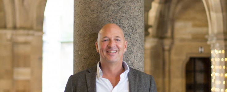 image of a man standing against a stone pillar at University of Glasgow cloisters