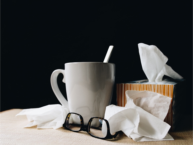 white mug beside eye glasses behind tissues on a black background
