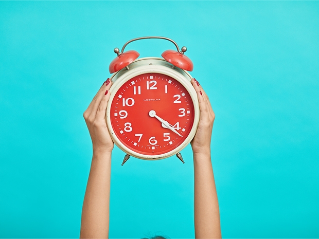 person holding red alarm clock against a blue background