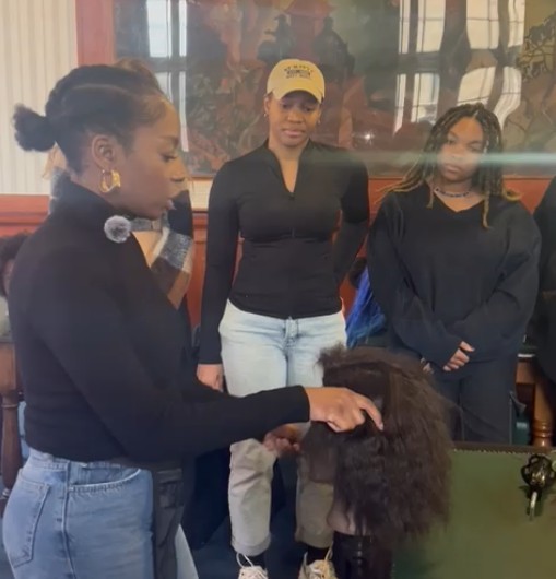 A group of students is practicing braiding and making cornrows on dolls in the Bridie Library of the Glasgow University Union, as part of the African Caribbean Society's braiding workshop.